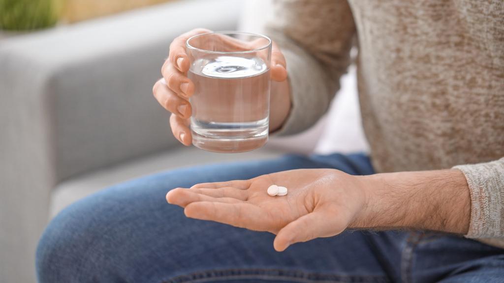 person taking tablets with glass of water at home close up